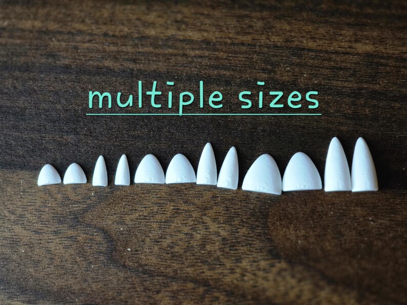 May include: A collection of twelve white, pointed, tooth-like plastic components arranged in a row, varying in width and height. The text "multiple sizes" is printed in light blue above the objects, which feature subtle, molded vertical lines.