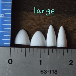 May include: Four white, pointed, three-dimensional objects with a visible wood grain texture, labeled 'large' in teal text. A metal ruler shows the objects range from approximately 0.5 to 1.5 inches in width along the bottom edge.
