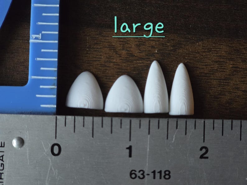 May include: Four white, pointed, three-dimensional objects with a visible wood grain texture, labeled 'large' in teal text. A metal ruler shows the objects range from approximately 0.5 to 1.5 inches in width along the bottom edge.