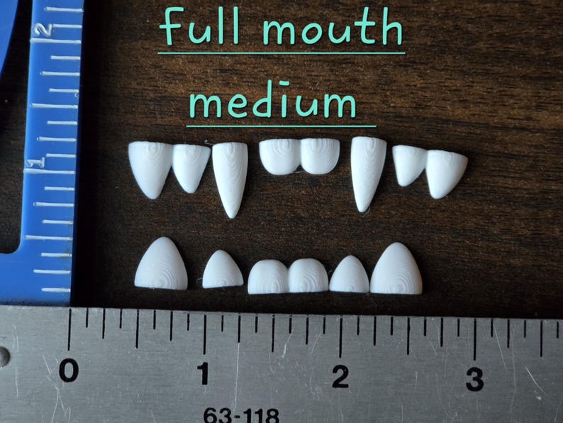 May include: A set of white, 3D-printed plastic teeth arranged in two rows, labeled full mouth medium. The teeth feature visible concentric circular textures. A blue plastic ruler and a metal ruler are visible, showing the set is approximately 2.5 inches wide.
