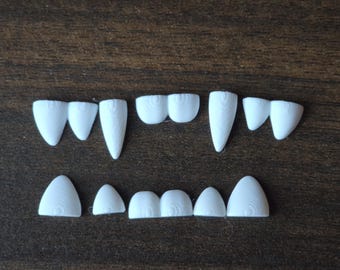 May include: A collection of white, 3D-printed plastic teeth arranged in two rows. The top row features pointed fangs and rounded incisors, while the bottom row consists of smaller, rounded teeth. Each piece displays a visible concentric layer texture.