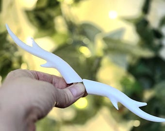 May include: A pair of white, smooth, branch-like antler accessories with pointed tips and small protrusions. The two pieces are separate, featuring a curved, organic shape that mimics the appearance of natural deer antlers in a solid white finish.