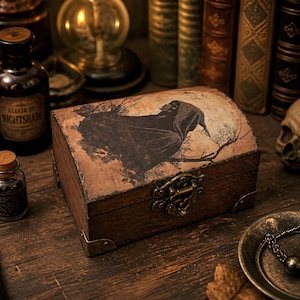 May include: A rectangular wooden box with a domed lid featuring a dark illustration of a hooded figure against a full moon. The box has a brass-coloured metal latch and corner reinforcements. The wood has a dark, weathered finish and texture.
