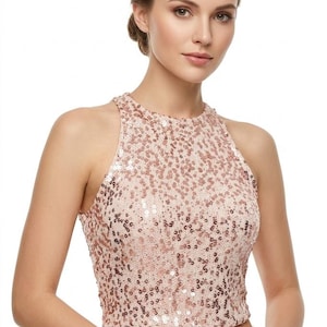 Puede incluir: Top halter con lentejuelas rosa claro. El top sin mangas tiene un cuello alto. Las lentejuelas pequeñas y muy juntas crean un efecto brillante. La parte inferior del top es de color liso. La modelo lleva pantalones blancos.