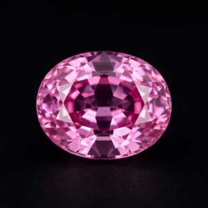 Puede incluir: Una gema de color rosa vibrante tallada en forma ovalada con múltiples facetas que reflejan la luz. La piedra muestra un tono magenta intenso en el centro, que se transforma en tonos de rosa más claros hacia los bordes, mostrando una estructura cristalina clara.