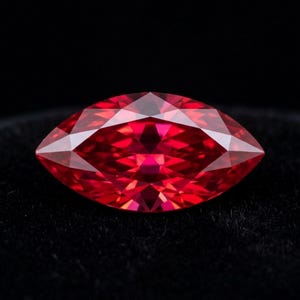 May include: A marquise-cut gemstone with a vibrant red color and a faceted surface that reflects light. The stone features a pointed oval shape with symmetrical edges, showcasing deep crimson tones and clear internal clarity throughout the piece.