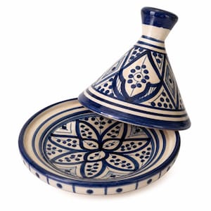 May include: A ceramic tagine, a traditional Moroccan cooking pot, with a conical lid. The tagine features a cream-coloured base and lid, adorned with intricate blue geometric and floral patterns. The lid is slightly ajar, revealing the interior.