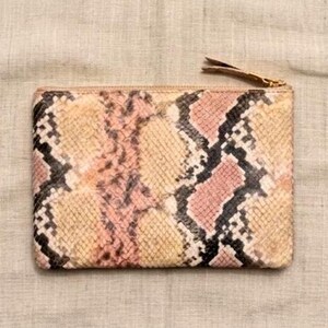 Puede incluir: Un estuche rectangular con cremallera que presenta un patrón de piel de serpiente texturizado en tonos rosa suave, beige y negro. El accesorio tiene un perfil delgado con un tirador de cremallera metálico en la esquina superior derecha con escamas.