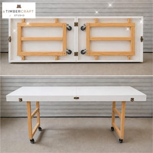May include: A white folding table with a smooth rectangular top and light wood legs. The table features metal hinges and black caster wheels on the base. The top section shows the underside structure with wooden supports and folding mechanisms.