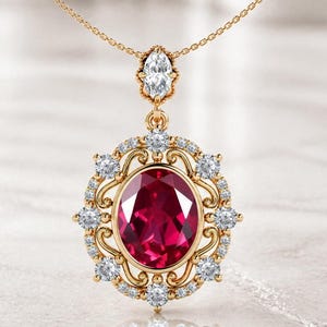 May include: A gold pendant necklace featuring a large oval ruby gemstone surrounded by small diamonds. The pendant has an ornate, filigree design with a smaller diamond at the top. The chain is delicate and gold.