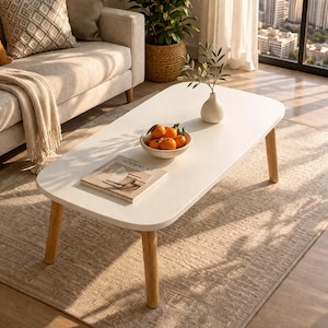 May include: A white oval coffee table with light wood legs. A bowl of oranges, a vase with greenery, and a book titled "MINIMALIST" are on the table. The table is in a living room setting.