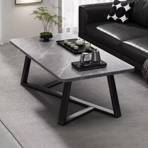 May include: A rectangular coffee table with a gray marble-look top and black metal legs. The table has a modern design and is placed on a gray rug. Decorative items, including a plant, tea set, and glassware, are arranged on the table.
