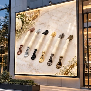 May include: Six elongated cabinet handles arranged in a row, each featuring a smooth cream-colored central bar and decorative metallic ends. The finishes on the ends include copper, silver, black, gold, dark gray, and antique bronze.