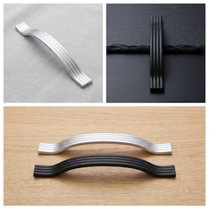 May include: A set of curved cabinet handles featuring a ribbed texture. The collection includes a silver-toned handle and a matte black handle, both designed with a consistent grooved pattern along the length of the hardware for a tactile grip.