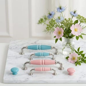 May include: A collection of cabinet hardware including two blue and two pink ceramic drawer pulls with silver metal bases, plus one small blue and one small pink round ceramic knob, all featuring a smooth, glossy finish and ribbed centre.