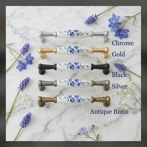 May include: Five cabinet pulls with white ceramic centers featuring blue leaf patterns. The hardware finishes include chrome, gold, black, silver, and antique brass. Each pull is labeled with its respective finish name in blue text.