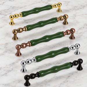 May include: Five cabinet pulls arranged in a row, each featuring a central green ceramic rod with a bamboo-like texture. The metal ends and mounting posts come in five distinct finishes: polished gold, antique brass, copper, chrome, and matte black.