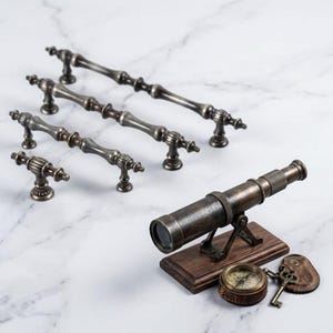 May include: Three antique brass-toned metal drawer pulls of varying lengths, one small brass-toned knob, a handheld telescope mounted on a rectangular wooden base, a round brass-toned compass, and a metal key attached to a leather tag.