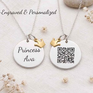 Op de afbeelding: Twee zilveren kettingen met ronde hangers. Eén hanger is gegraveerd met "Princess Ava" en een gouden kroonbedel. De andere hanger heeft een QR-code en een gouden kroonbedel. De tekst "Laser-Engraved & Personalized" staat bovenaan.
