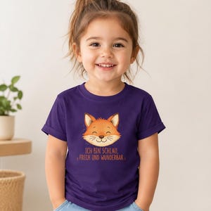 Könnte beinhalten: Ein dunkelviolettes Kurzarm-T-Shirt mit einer Grafik eines lächelnden orangefarbenen Fuchskopfes. Unter dem Fuchs steht der Text "ICH BIN SCHLAU, FRECH UND WUNDERBAR" in orangefarbenen Buchstaben. Das T-Shirt hat einen Rundhalsausschnitt und Ärmelaufschläge.