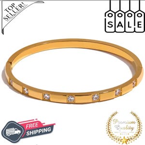 Op de afbeelding: Een goudkleurige armband met vierkante heldere kristallen. De armband heeft een eenvoudig, elegant ontwerp. De afbeelding bevat ook de woorden "Top Seller!" en "SALE".
