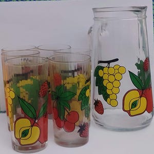 Puede incluir: Una jarra de cristal transparente y cuatro vasos a juego. Cada pieza está decorada con ilustraciones de frutas coloridas, incluyendo uvas, manzanas, cerezas y fresas. La jarra tiene un asa y una abertura ancha, perfecta para servir bebidas.