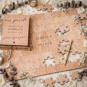 May include: A wooden wedding guest book puzzle with the text "our puzzle would not be complete without you please sign a piece". The puzzle is personalized with the names "Jessica and Oliver" and the date "08.09.2027".