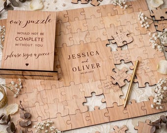 May include: A wooden wedding guest book puzzle with the text "our puzzle would not be complete without you please sign a piece". The puzzle is personalized with the names "Jessica and Oliver" and the date "08.09.2027".