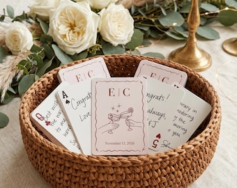 May include: A round, brown, hand-crocheted basket filled with a deck of rectangular white cards. The top card features the initials E|C, an illustration of two hands clinking cocktail glasses, and the date November 13, 2026, in black text.