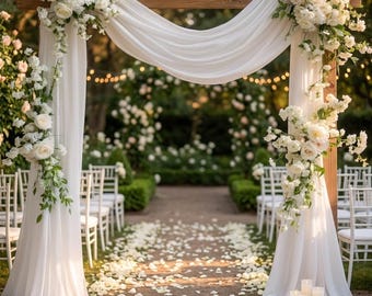 May include: A wooden wedding arch draped with flowing white fabric and adorned with large clusters of white roses and greenery. The structure stands over a path covered in white flower petals, with white chairs arranged on both sides of the aisle.