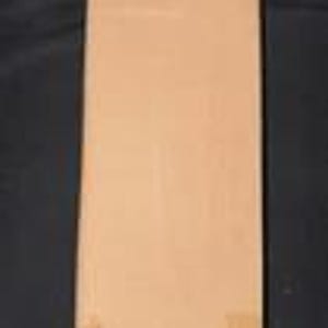 May include: A rectangular, light brown book with a plain cover. The book is standing upright against a dark background. The cover has a smooth texture and appears to be made of paper or cardboard. There are small, light-colored marks on the bottom right corner.