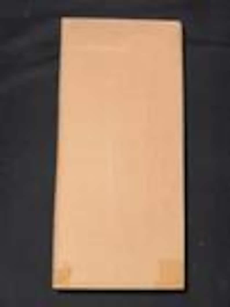May include: A rectangular, light brown book with a plain cover. The book is standing upright against a dark background. The cover has a smooth texture and appears to be made of paper or cardboard. There are small, light-colored marks on the bottom right corner.
