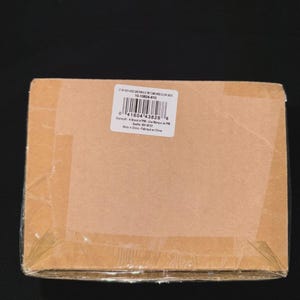 May include: A sealed cardboard box, wrapped in clear plastic, with a white label featuring a barcode and text. The box is brown and taped shut. The label includes the text "10-10624-810".