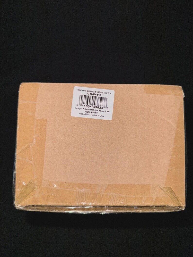 May include: A sealed cardboard box, wrapped in clear plastic, with a white label featuring a barcode and text. The box is brown and taped shut. The label includes the text "10-10624-810".