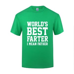 Puede incluir: Una camiseta de manga corta de color verde brillante con letras blancas en bloque en el pecho que dicen: WORLD'S BEST FARTER I MEAN FATHER. La prenda tiene cuello redondo y un corte estándar, mostrando un texto claro y centrado al frente.