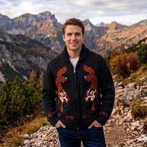 May include: A dark grey zip-up cardigan with a shawl collar and a brown and white deer design. The cardigan is worn over a white shirt. The background features a mountain range and trees.