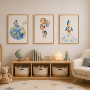 May include: A nursery scene with three framed watercolor prints featuring space themes: an astronaut on Earth, planets with an astronaut, and a rocket. The room includes a crib, a bookshelf, a chair, and a star-shaped rug.