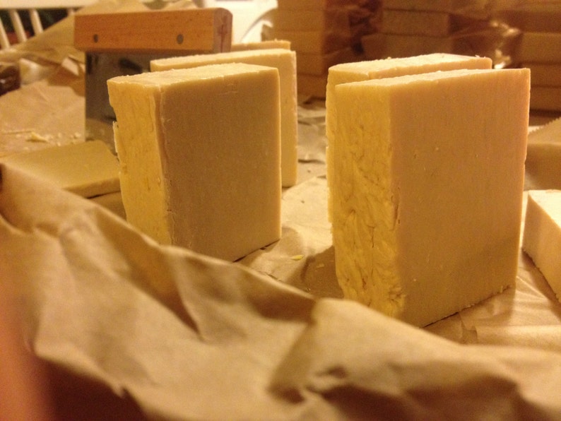 May include: Four bars of white soap on a brown paper surface. The soap bars are rectangular and have a smooth, slightly textured surface.