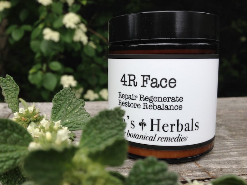 May include: A jar of 4R Face botanical remedy with a black lid and a white label. The label includes the text "Repair Regenerate Restore Rebalance" and "Lee's Herbals botanical remedies". The jar is set against a backdrop of green foliage.