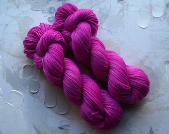 May include: Two skeins of bright pink yarn, twisted together, on a textured white background.