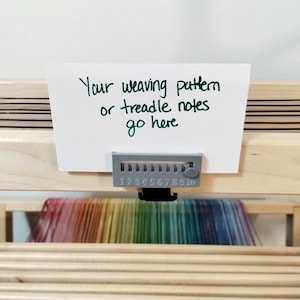 May include: A white card with the text "Your weaving pattern or treadle notes go here" attached to a wooden loom with a numbered counter. The counter has numbers 1 through 10.