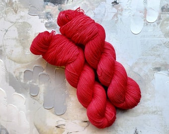 May include: A skein of vibrant red yarn, tightly twisted and braided, rests against a textured, abstract background with white and gray brushstrokes. The yarn's color is a bold, saturated red, perfect for knitting or crochet projects.