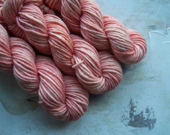 May include: A close-up of a skein of pink and white yarn. The yarn is soft and fluffy, and it has a subtle sheen.