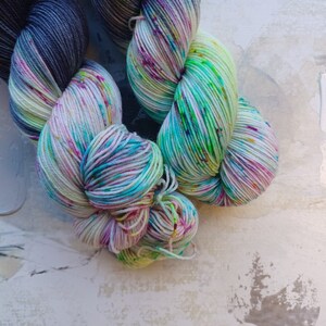 Pode incluir: Dois novelos de fio, um &eacute; um degrad&ecirc; azul escuro e cinza, o outro &eacute; uma base branca com respingos de rosa, verde e azul.