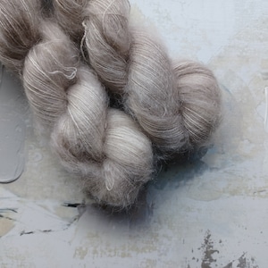 Peut inclure: Deux écheveaux de fil doux gris clair avec une texture duveteuse. Le fil est torsadé et semble être composé d'un mélange de fibres.