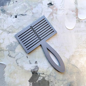 Puede incluir: Un peine de plástico gris con mango. El peine tiene una serie de líneas paralelas y una línea diagonal de agujeros.