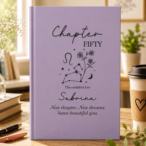 May include: A lavender journal with the words "Chapter FIFTY" and "Sabrina" in black script. The cover features a Leo constellation design and the text "New chapter. New dreams. Same beautiful you."