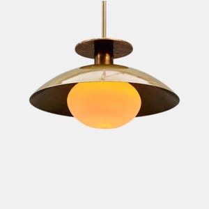 May include: A brass-colored pendant light fixture with a rounded shade and a spherical, glowing orange light bulb. The fixture is suspended from a thin rod, creating a modern and elegant design. The light fixture is suitable for indoor use.