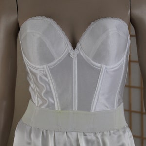 Op de afbeelding: Witte strapless bh met beugels en een satijnen afwerking. De bh heeft een gladde, naadloze cup en een brede band.