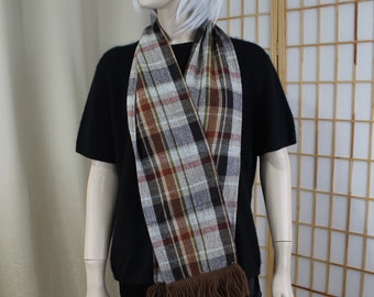 May include: A brown, gray, and red plaid scarf with brown fringe. The scarf is worn around the neck of a mannequin.